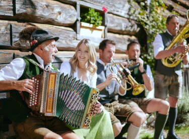 Musikanten in Tracht spielen ihre Instrumente vor einer Berghütte