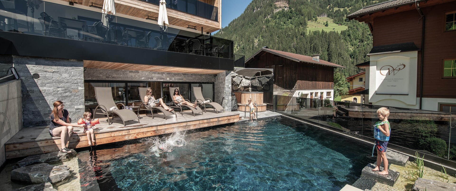 Naturpool mit spielenden Kindern und Liegestühlen vor dem B&B Hotel Das Diellehen im Sommer.