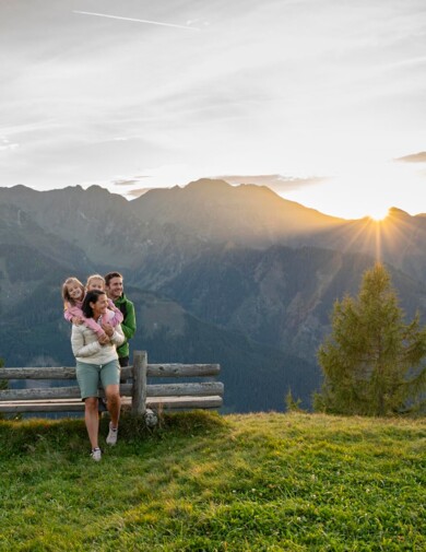 Eine Familie steht beim Sonnenuntergang am Berg und hat viel Spaß.