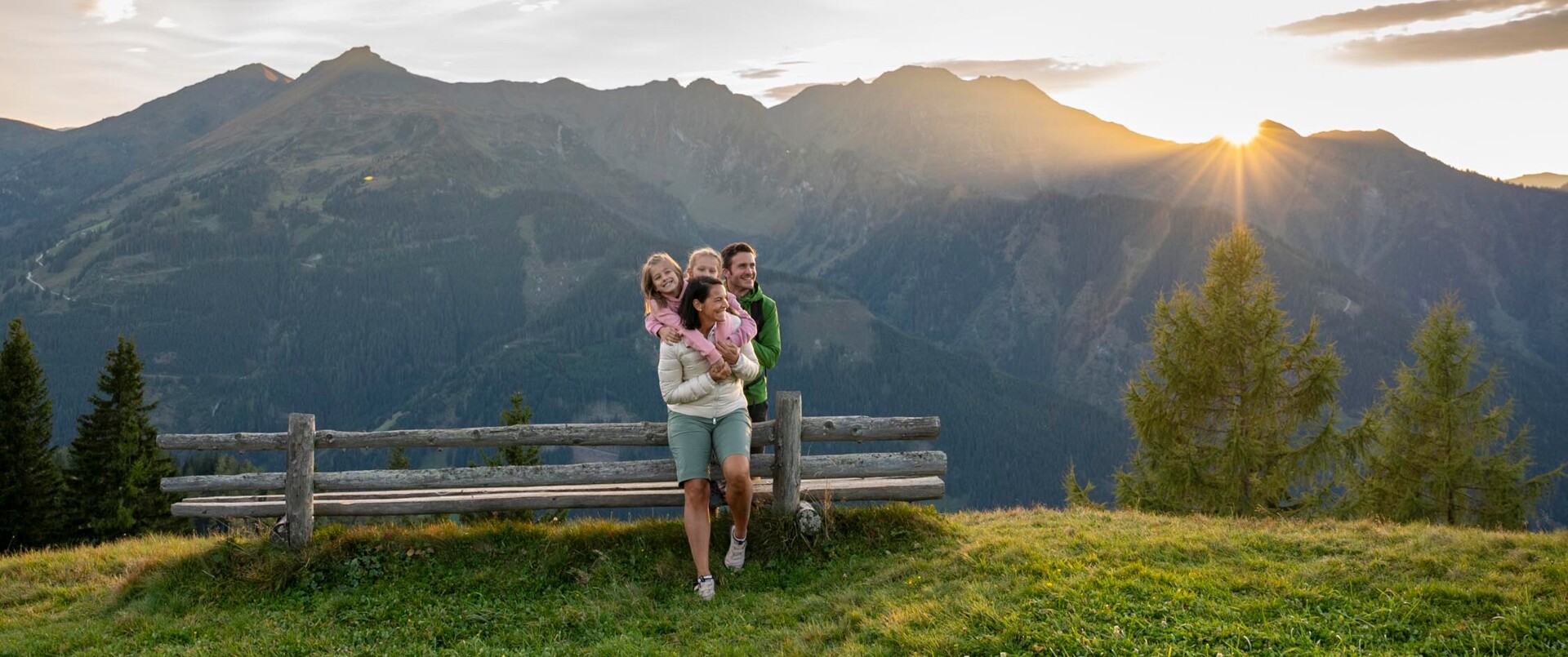 Eine Familie steht beim Sonnenuntergang am Berg und hat viel Spaß.