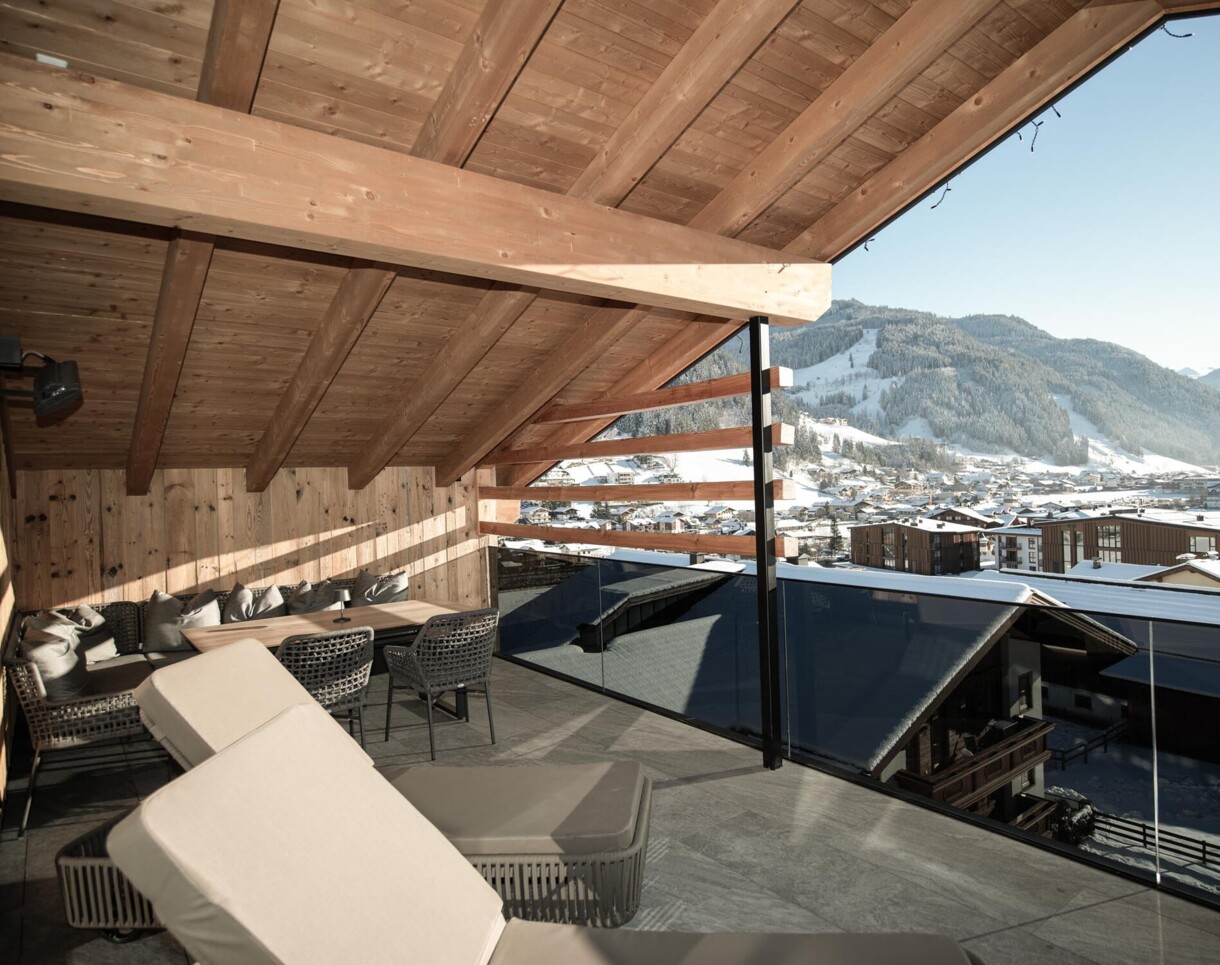 Großzügiger Balkon mit Liegestühlen und Blick auf verschneite Berge und ein Dorf im Hotel Diellehen.