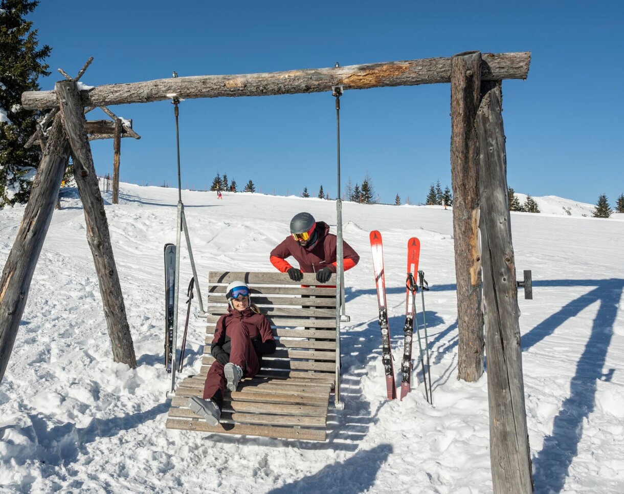 Eine Frau liegt in einem Schaukelstuhl inmitten des Skigebietes und genießt die Sonne