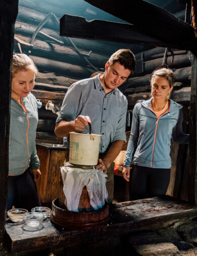 Ein Senner zeigt zwei interessierten Gästen, wie man auf der Alm in Großarl Käse macht.