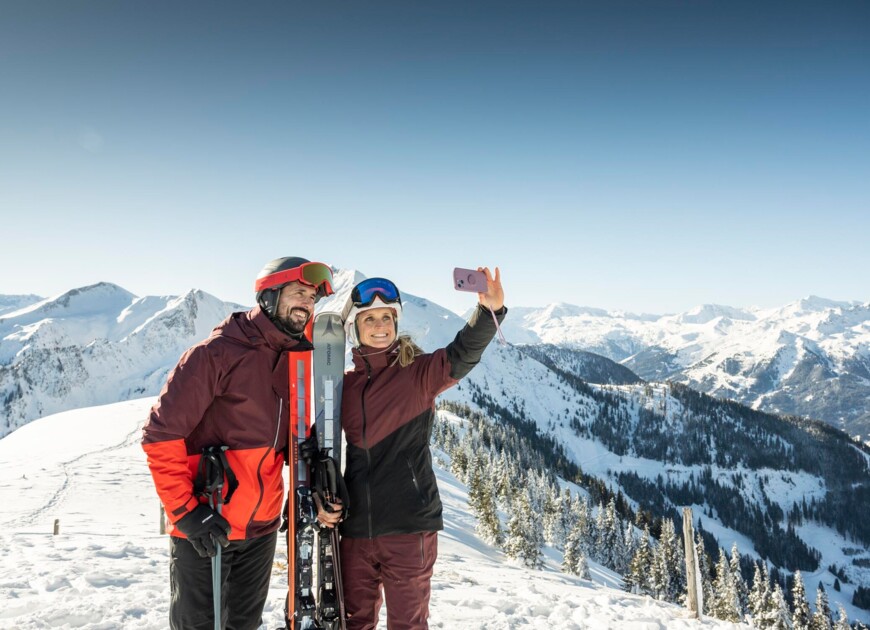 Ein Paar steht am Gipfel des Berges und macht ein Selfie von sich und der winterlichen Landschaft in Großarl.