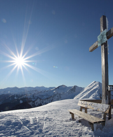 Strahlender Sonnenschein und blauer Himmel am Gipfel des Berges mit einem Gipfelkreuz.