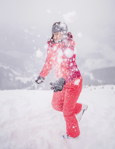 Person in roter Winterkleidung spielt fröhlich im Schnee.