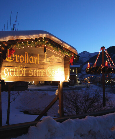 Beleuchtetes Holzschild und Lichterdekoration bei Dämmerung im verschneiten Bergdorf Großarl.